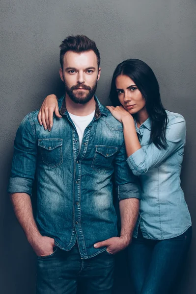 Young couple in jeans wear standing close to each other and looking at camera with grey background