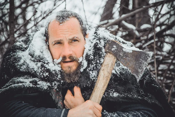 Portrait of a Bearded Man with an ax in his hand. Brutal bearded man with an ax. North bearded man with an ax in the woods.
