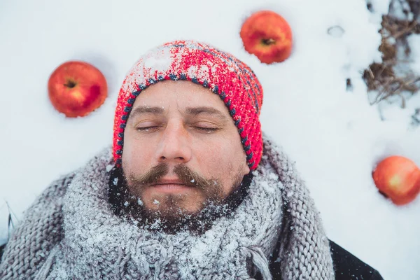 The face of a bearded man lying in the snow under the apple tree. Close up portrait of a bearded man near the apple tree in the winter.