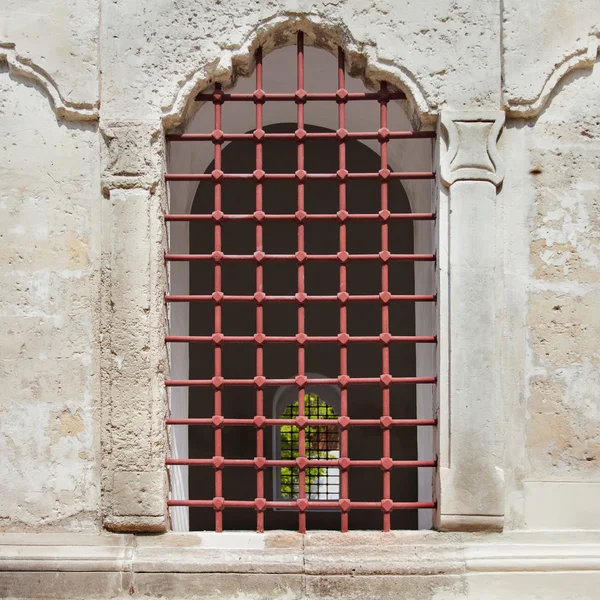 Old arch window with metal grid in a stone wall