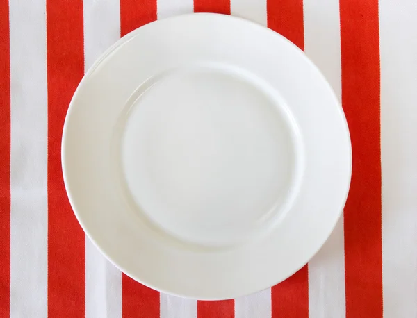 White empty plate on red striped tablecloth.