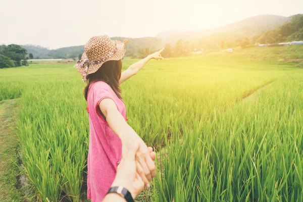 Young woman holding man hand and leading on the rice greenfield