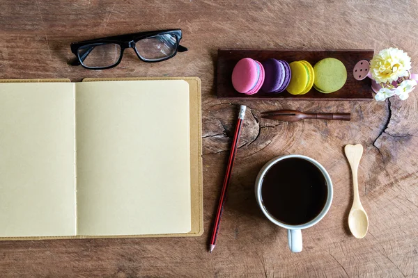 Colorful macaroons and a cup of coffee with notebook on wooden t