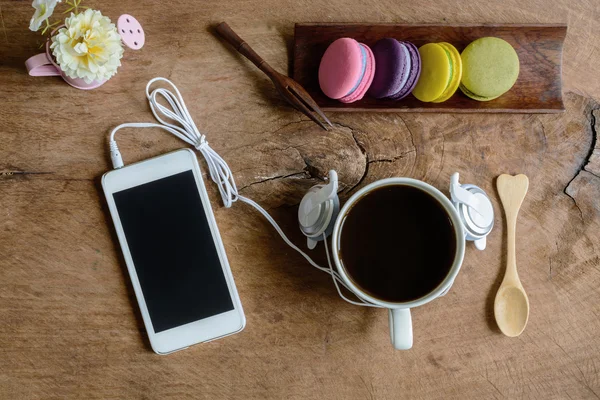 Colorful macaroons and a cup of coffee with cellphone on wooden