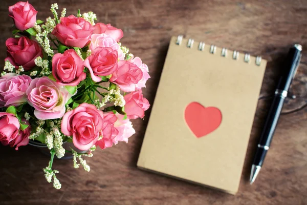 Flower with blank notepad and pen on old wooden background