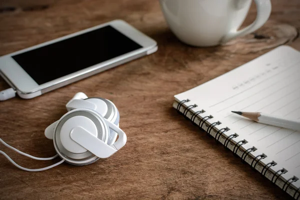 Earphone with coffee and notebook on old wooden table
