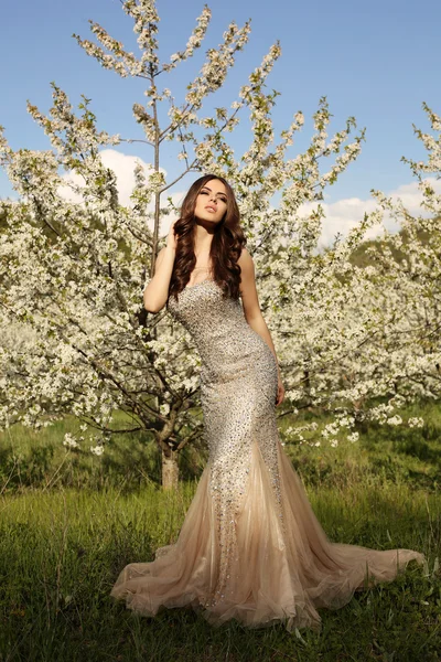 Sensual woman with dark hair in elegant dress posing in blossom garden