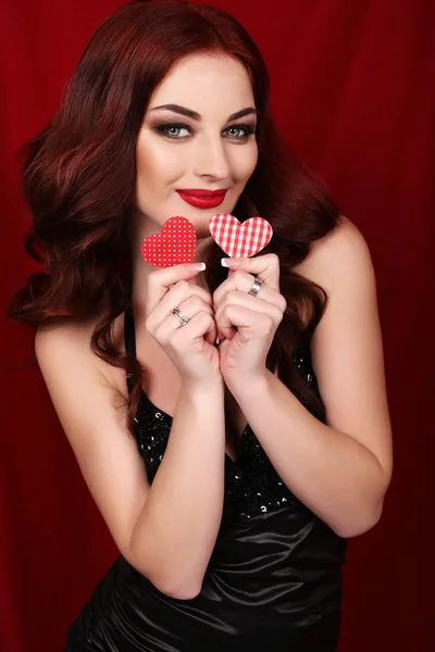 Woman with dark hair and bright makeup posing with red heart , symbol of love and Valentine\'s day