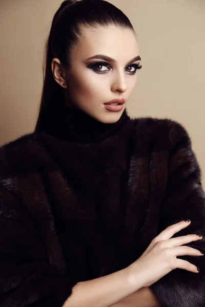 Beautiful young woman with dark hair and evening makeup, wears elegant fur coat