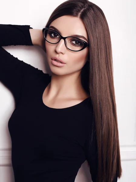 Businesslike woman with long dark hair wears elegant black dress and glasses