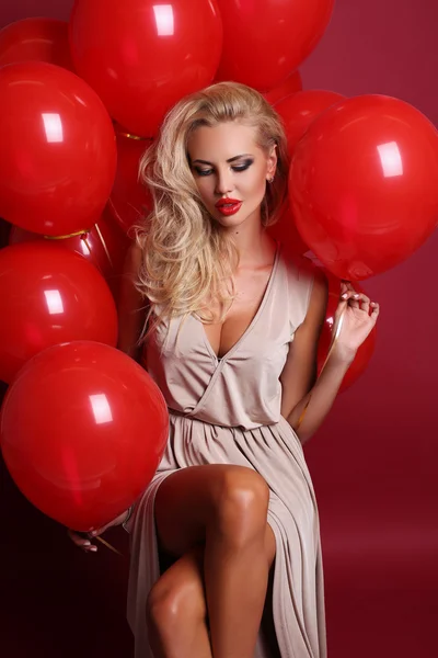 Sexy woman with blond curly hair wears elegant dress, holding a lot of red air balloons
