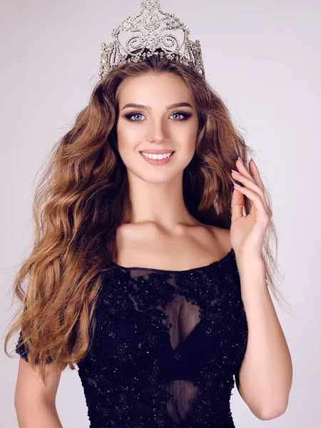 Gorgeous young woman with dark hair in luxurious dress with precious crown