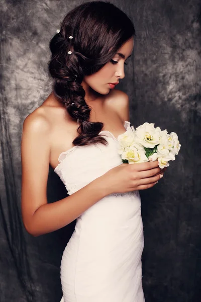 Beautiful bride with dark hair in elegant wedding dress with bouquet of flowers