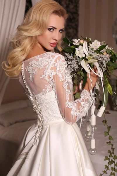 Gorgeous woman with blond hair wears luxurious wedding dress and bijou
