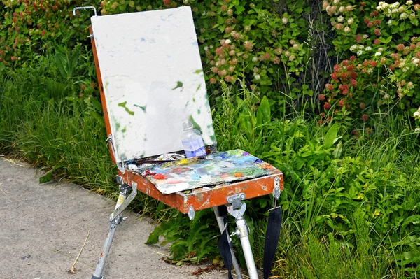 Hands of the artist with a brush, paint a picture on an easel in the open air