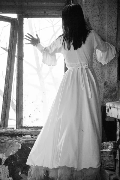 Sad mood in an old, abandoned house with girl wearing an old fashioned wedding dress with natural light. Photo has grain texture visible on its maximum size. Artistic black and white photography