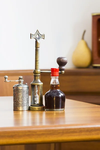 Still life composition with metallic pepper grinder, small bottle of aromatic vinegar and copper corkscrew on wooden table