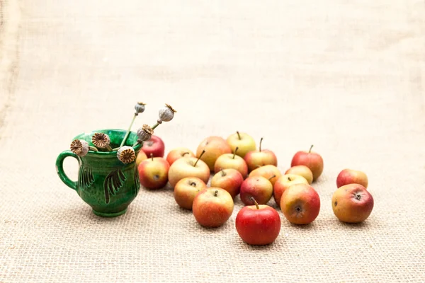 Small, red apples and ceramic cup with poppy seeds with burlap texture in the background