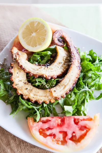 Grilled octopus on lettuce leaves with lemon and tomato slice
