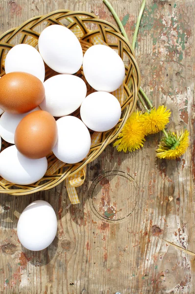 Eggs in a wicker basket on wooden background. Eggs in a wicker basket and dandelions on wooden background, top view