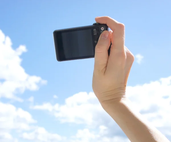 Hand holding digital camera. Girl\'s hand with the camera against the sky. Empty space for your picture or text.