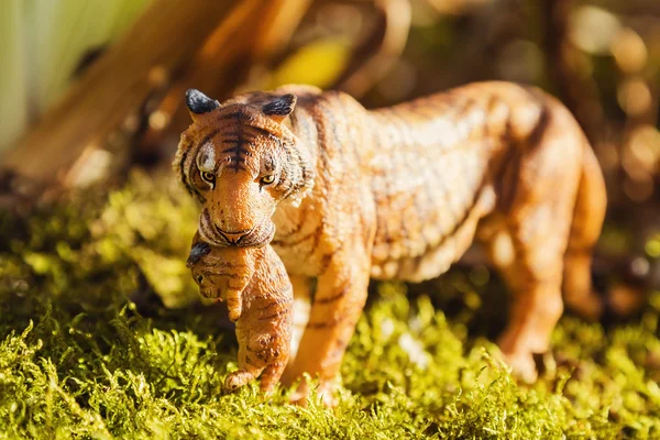 Tigress with cub in teeth. Tiger toy figurine in situation.