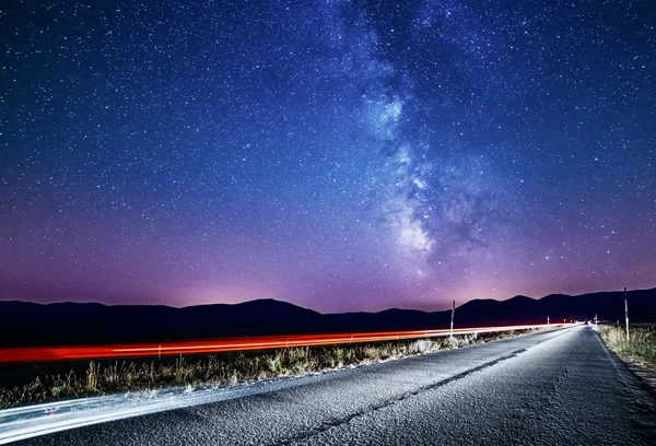 Night sky with milky way and stars. Night road illuminated by car