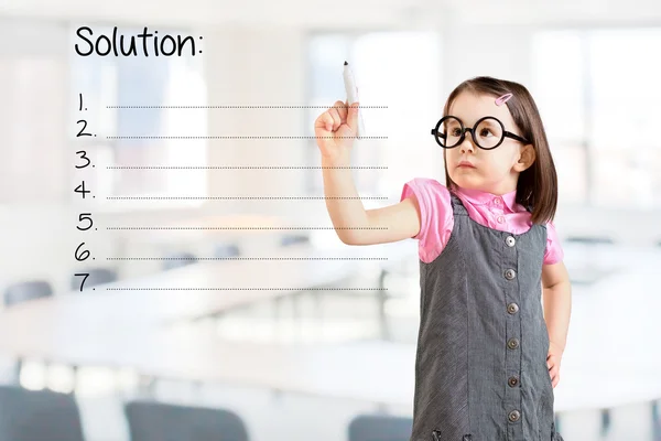 Cute little girl wearing business dress and writing blank solution list. Office background.