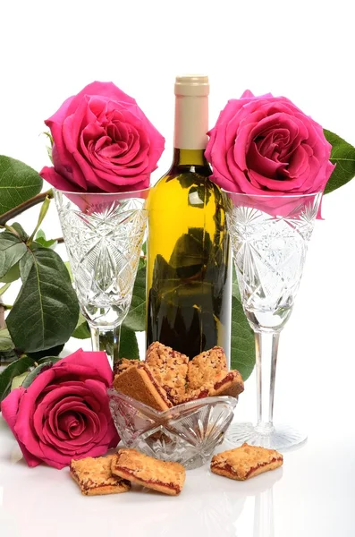 Crystal glasses, a bottle of wine, cookies and a bouquet of roses in a still life