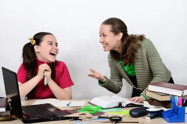 Female teacher and schoolgirl teenager at a school desk socialize animatedly, are laughing, smiling.