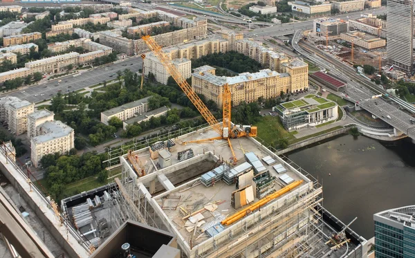 Construction of office high-altitude buildings. Construction crane on the roof of the tower on the background of the urban landscape. View from above