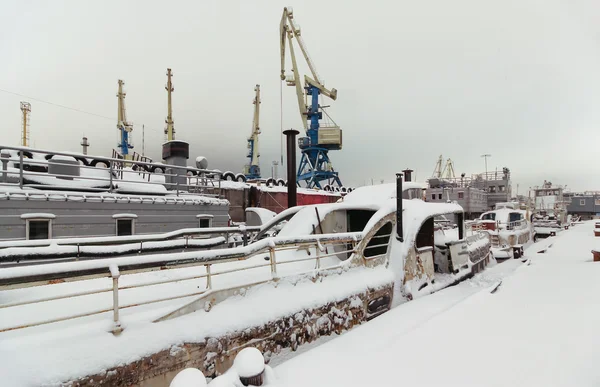 Night view of harbor cranes on the waterfront of the port covered with snow. Abandoned ships moored at the berth