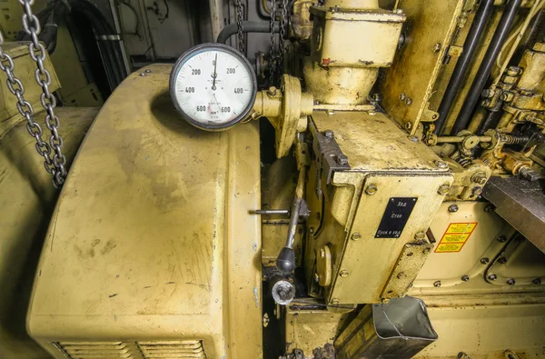 The ship\'s hold with yellow diesel engine mounted on ship. Engine room on a old cargo boat ship. The control panel with tachometer