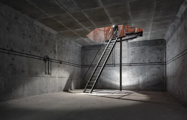 Concrete room under ground with a ladder to the surface from which the light comes. Technical room ventilation shaft of the underground facility