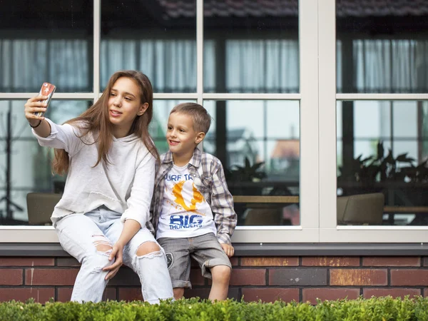 Smiling childrens make selfie sitting on the sill against the window