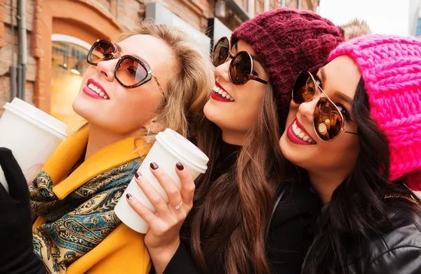 Close up portrait of three young cheerful pretty girls friends drinking coffee.  Smiling and going shopping.