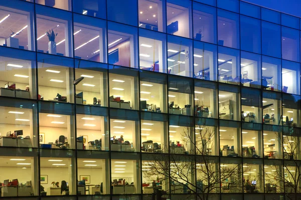 LONDON, UK - DECEMBER 19, 2014: Office block with lots of lit up windows and late office workers inside. City of London business aria in dusk.