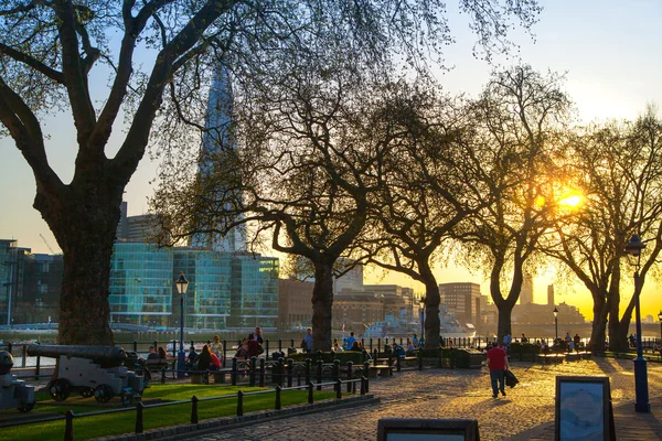 LONDON, UK - APRIL15, 2015: Tower park in sun set. River Thames side walk with people resting by the water