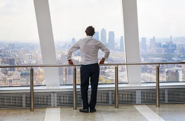 LONDON, UK - APRIL 22, 2015: Businessman looking at London through the window of Walkie-Talkie building. View includes Canary Wharf business and banking aria. Business concept image