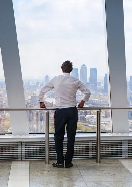 LONDON, UK - APRIL 22, 2015: Businessman looking at London through the window of Walkie-Talkie building. View includes Canary Wharf business and banking aria. Business concept image