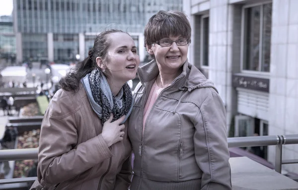 Outdoor family portrait of pension age Mother and her daughter in the city, smiling and looking around. Two generation, happiness and care concept