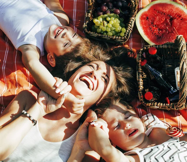 Cute happy family on picnic laying on green grass mother and kids, warm summer vacations close up, brother and sister