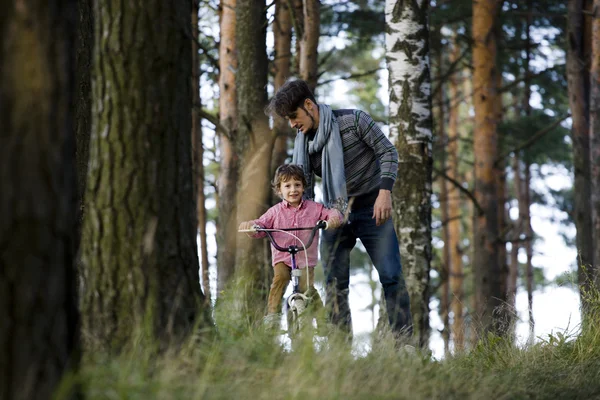 Father learning his son to ride on bicycle outside, real happy family in summer forest enjoing nature