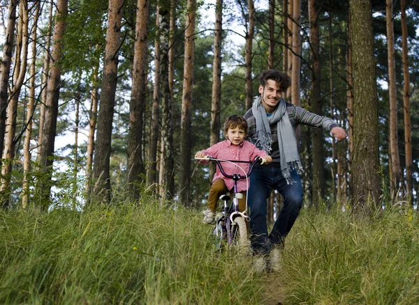 Father learning his son to ride on bicycle outside, real happy family in summer forest enjoing nature