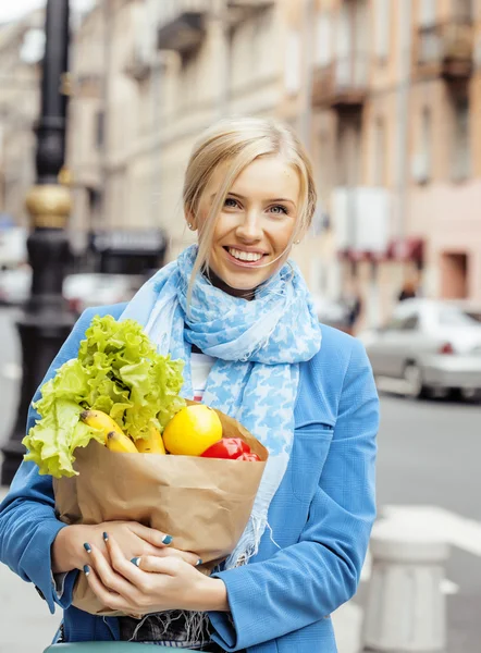 Young pretty blond woman with food in bag walking on street