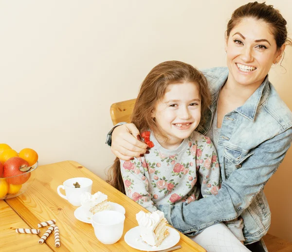 Young mother with daughter on kitchen drinking tea together hugging eating celebration cake