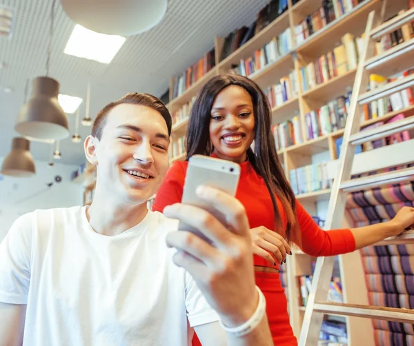 Couple students in univercity library, looking book, preparing to exam, having fun, making selfie