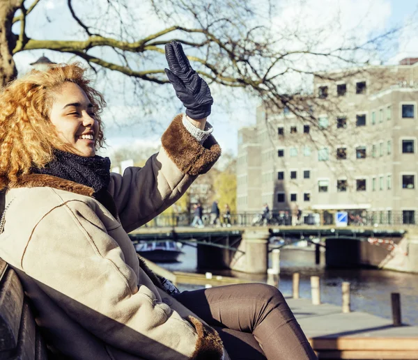 Cute pretty mulatto woman waving and smiling welcoming friends, streets of Amsterdam