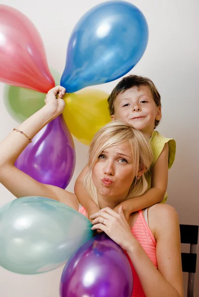 Pretty real family with color balloons on white background, blond woman with little boy at birthday party bright smiling mother