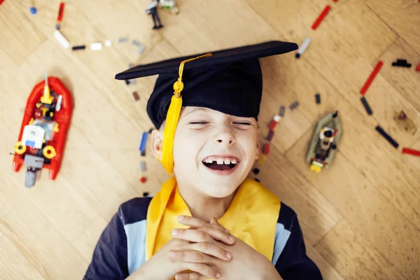 Little cute preschooler boy among toys lego at home in graduate hat smiling posing emotional, lifestyle people concept